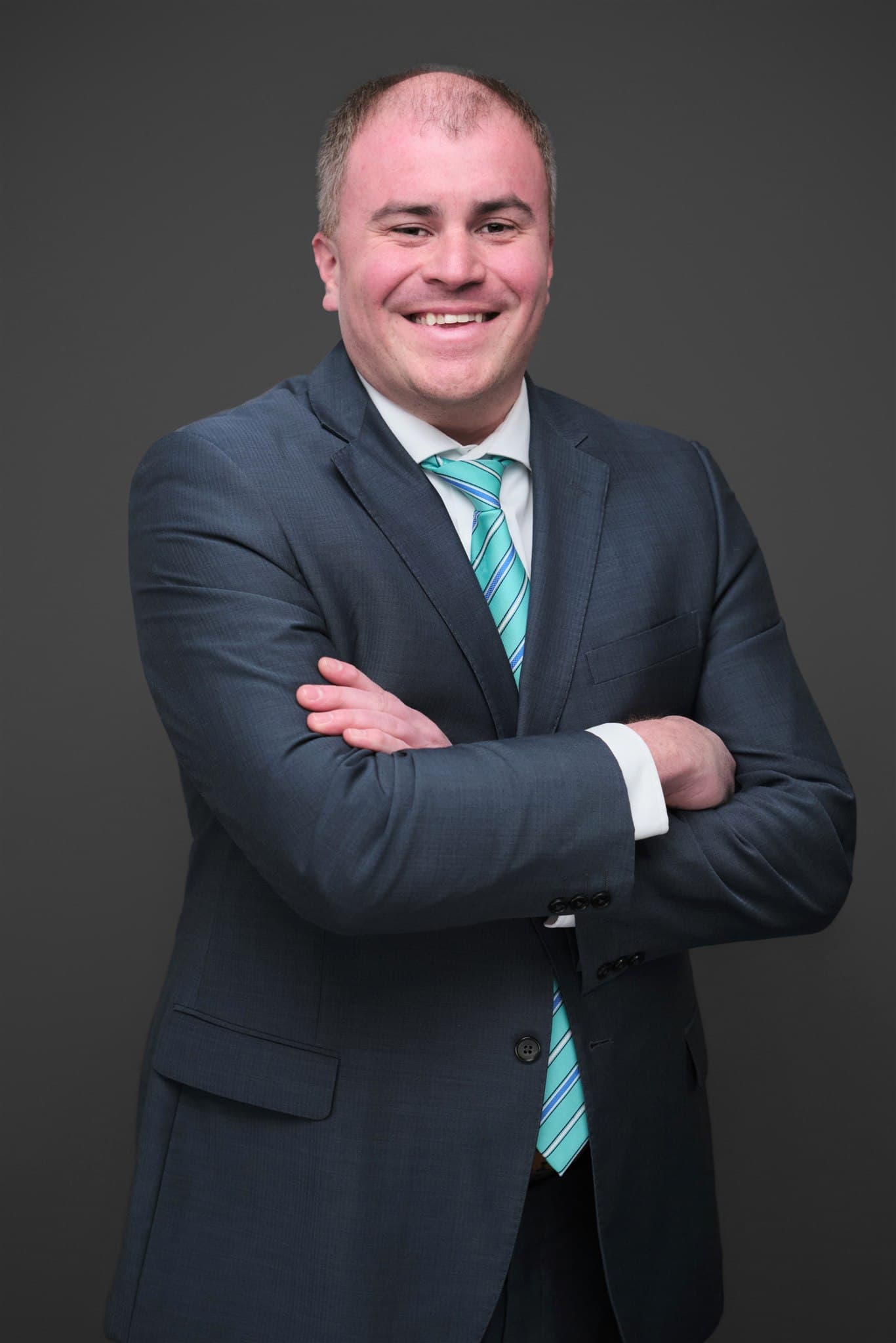 Smiling man with arms crossed in a gray suit and teal striped tie by Henry David Photography, the standard every Creve Coeur headshot session is held to