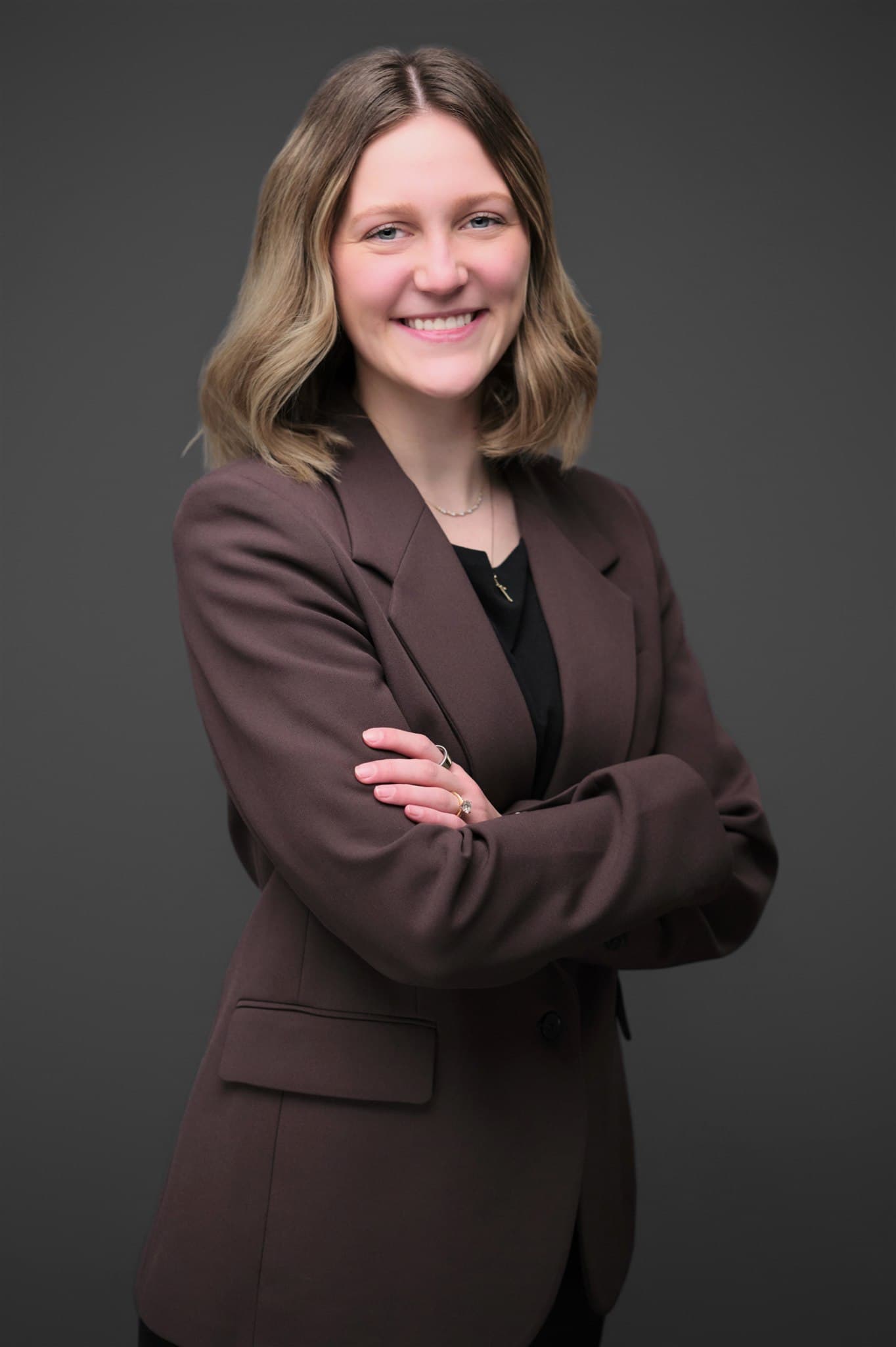 Smiling woman with arms crossed in a brown blazer, gray backdrop by Henry David Photography, the standard every St. Charles headshot session is held to