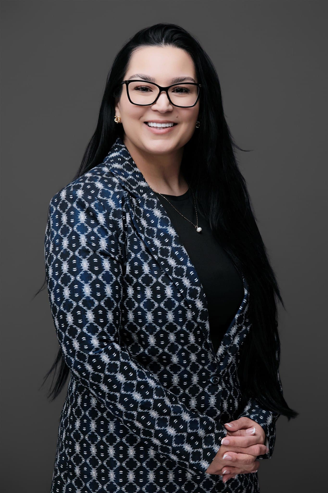 Woman in glasses and a patterned blue jacket, photographed on a dark studio backdrop