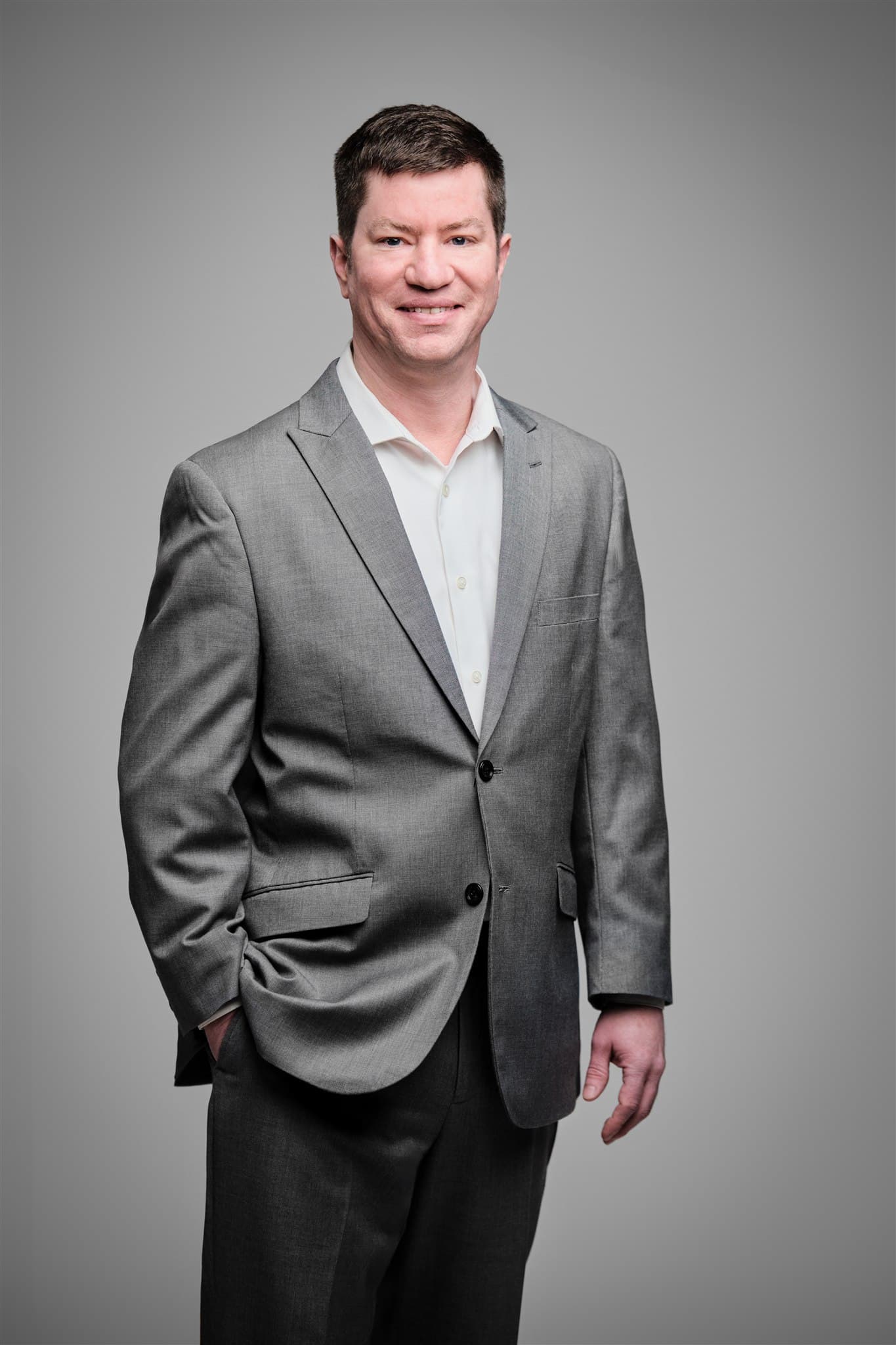 Approachable professional man in light gray suit and open-collar white shirt against a light gray backdrop by Henry David Photography