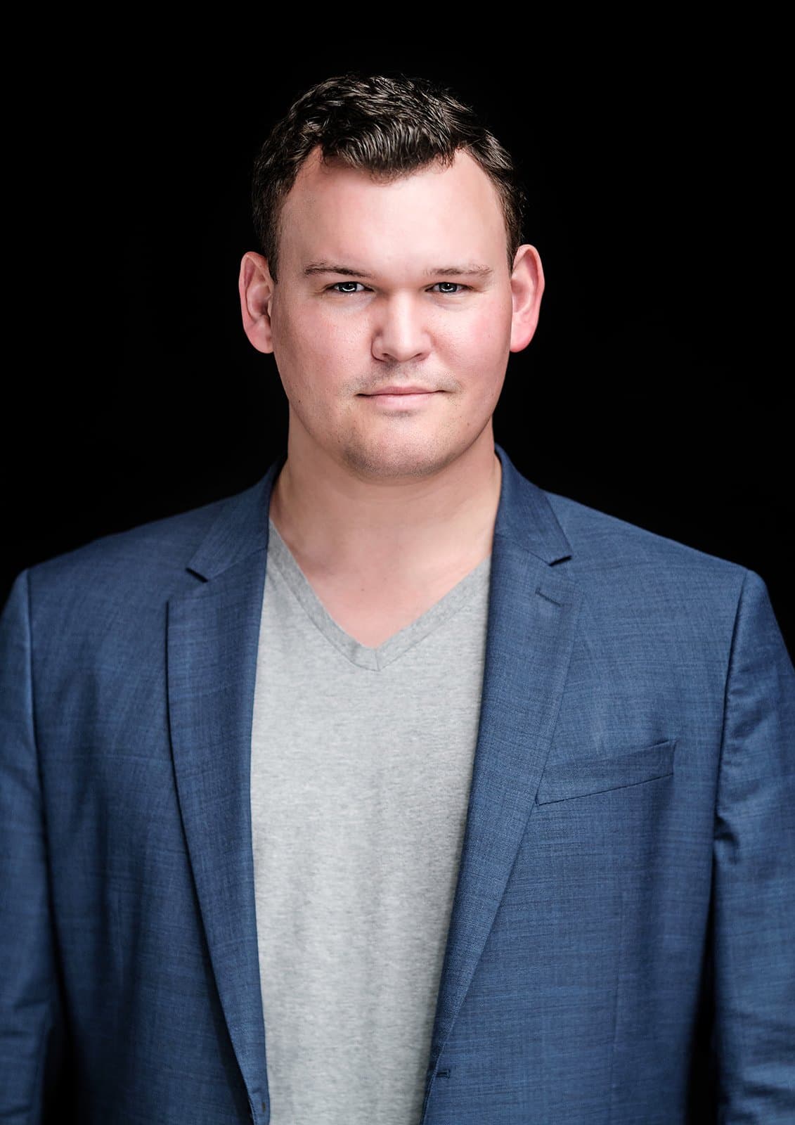 Man in a blue blazer over a gray v-neck on a black backdrop by Henry David Photography, the standard every Central West End headshot session is held to