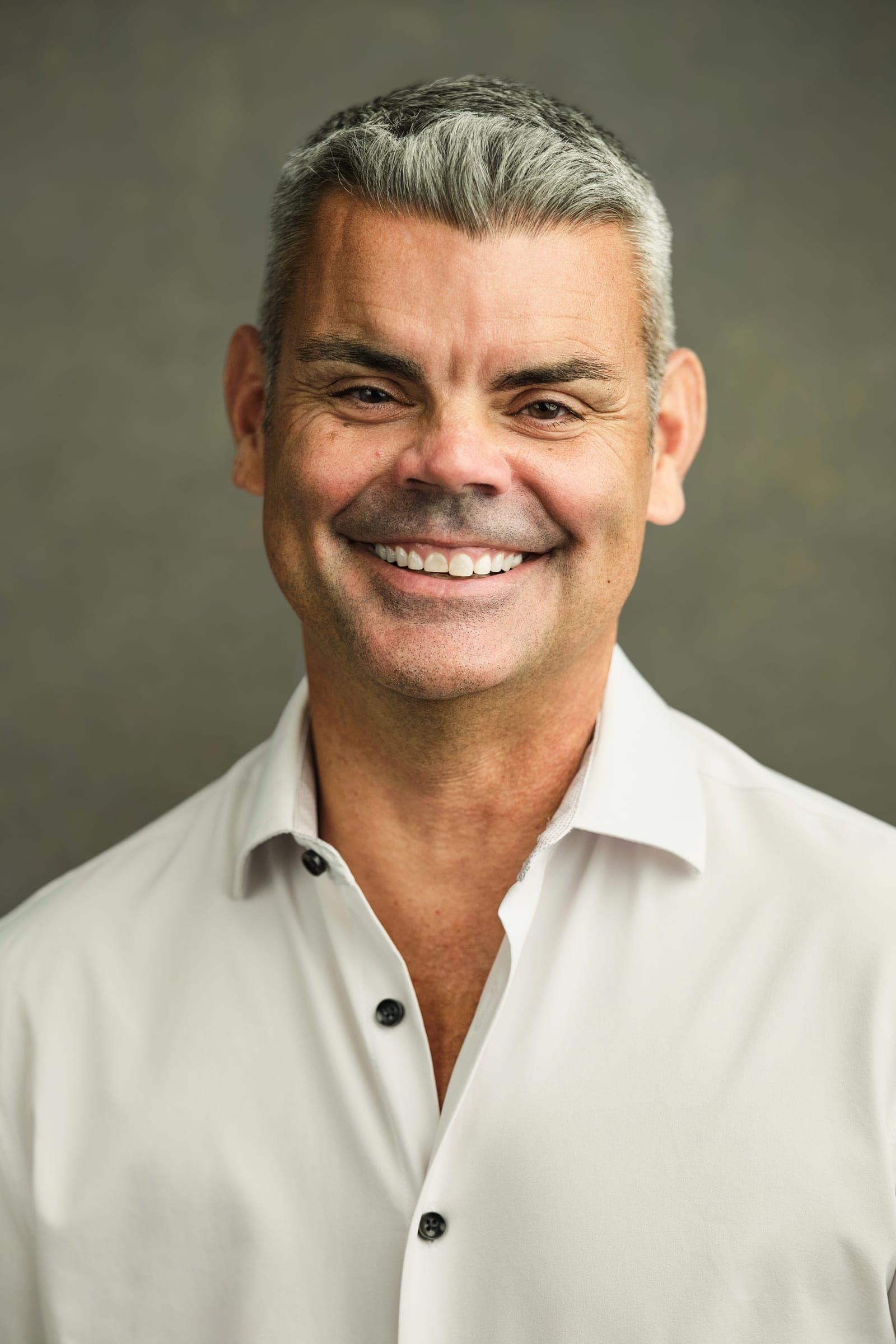 Daniel M. McLaughlin, member at Johnson & Krol, in an open-collar white shirt, headshot on the firm's green canvas backdrop at its St. Louis office in Des Peres by Henry David Photography