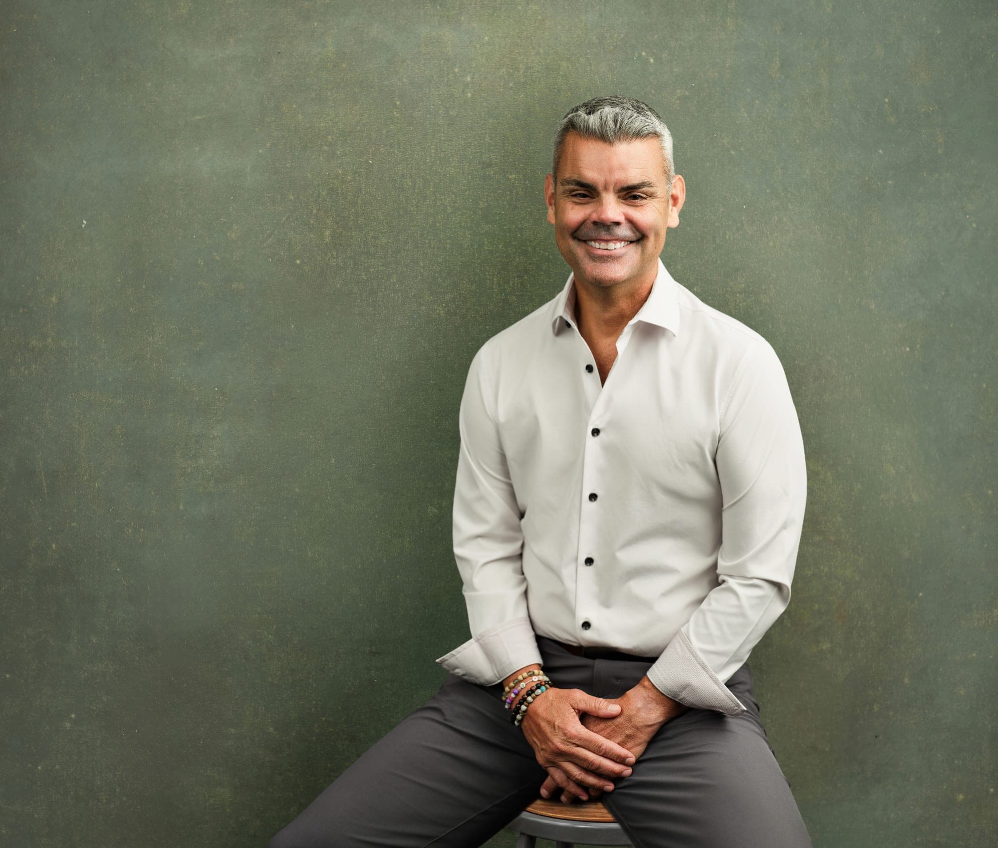 Daniel M. McLaughlin, member at Johnson & Krol, in a white shirt and charcoal trousers, seated three-quarter portrait against the firm's green canvas backdrop, at its St. Louis office in Des Peres by Henry David Photography