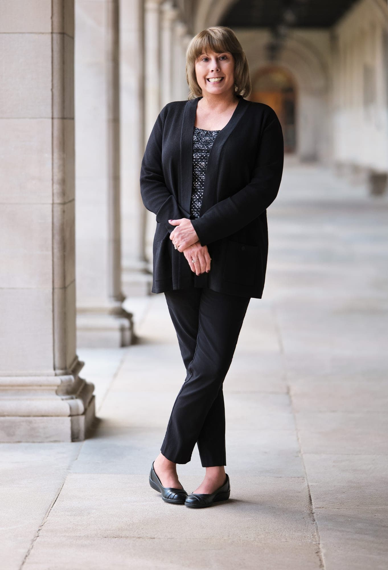 MHS Legacy team member in a black cardigan and trousers photographed in the limestone arcade at Washington University Brookings Hall by Henry David Photography