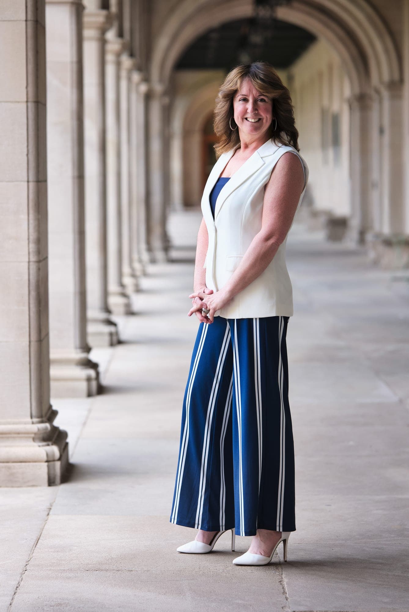 MHS Legacy executive in a white sleeveless blouse and striped wide-leg trousers framed by the limestone columns of the Brookings Hall arcade by Henry David Photography