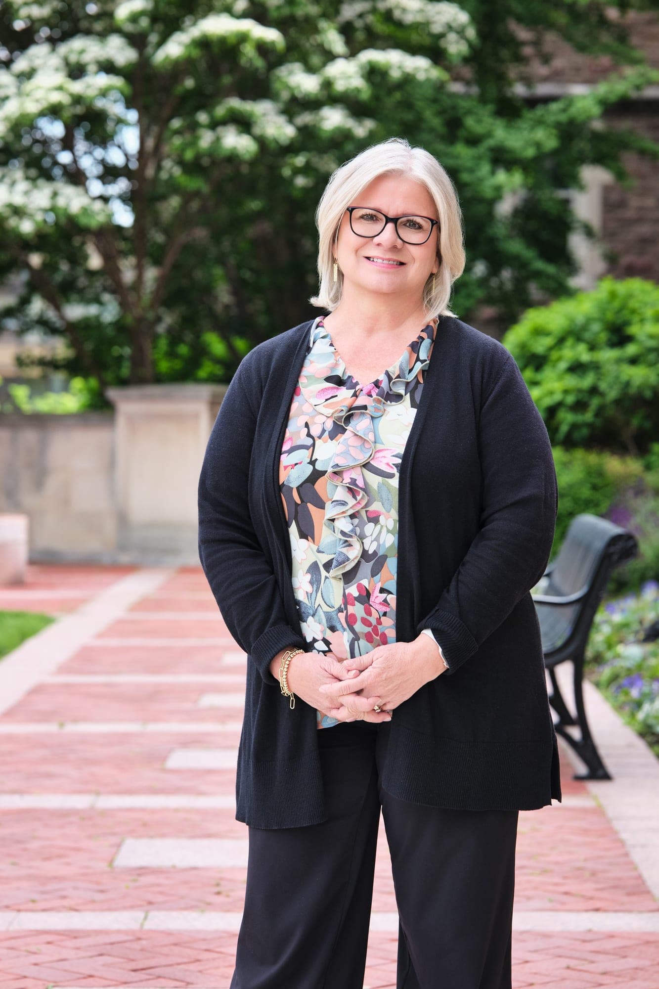MHS Legacy team member in a black cardigan over a watercolor floral blouse photographed on the brick garden path at Washington University Brookings Hall by Henry David Photography