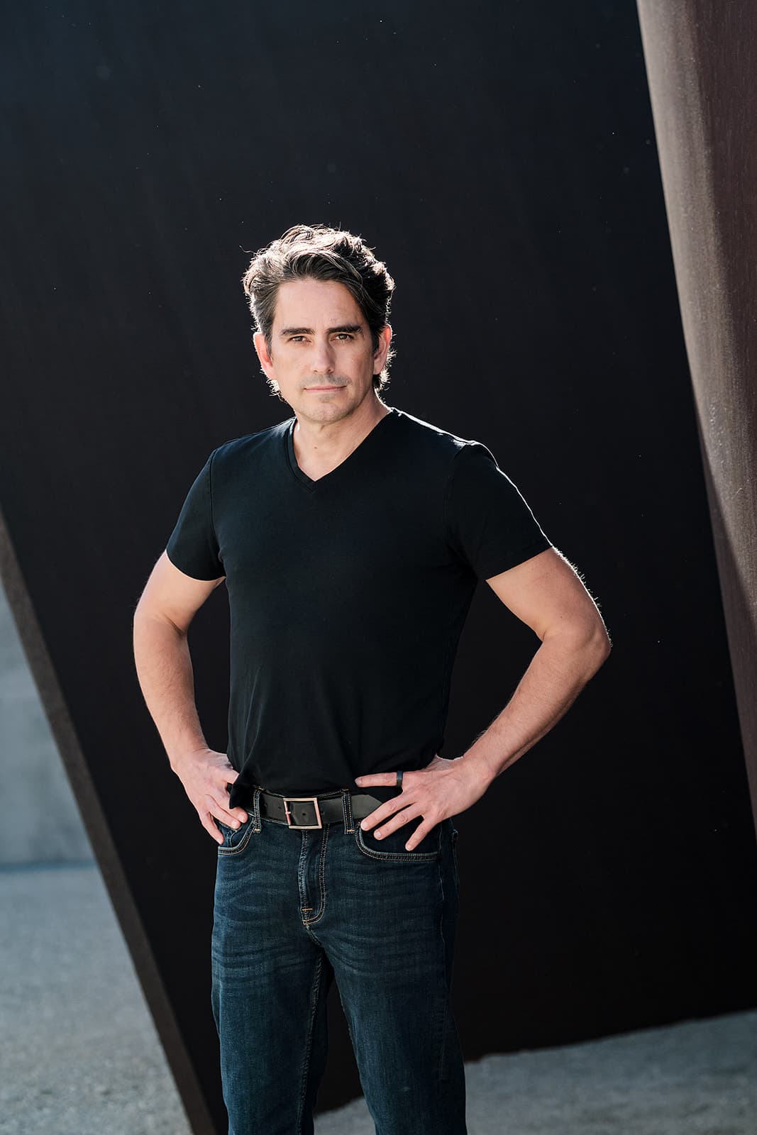 Outdoor portrait of a man in a black t-shirt and jeans by dark walls by Henry David Photography, the standard every Webster Groves headshot session is held to
