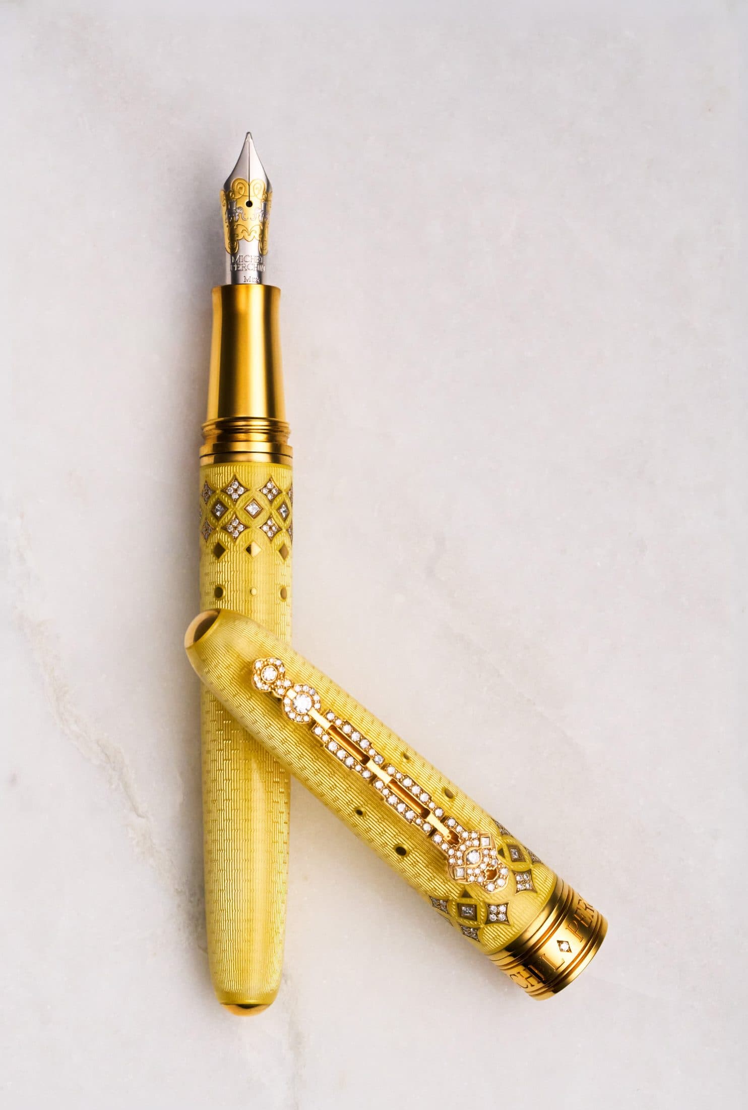 Two Michel Perchin Majesty yellow guilloche enamel fountain pens crossed on Carrara marble