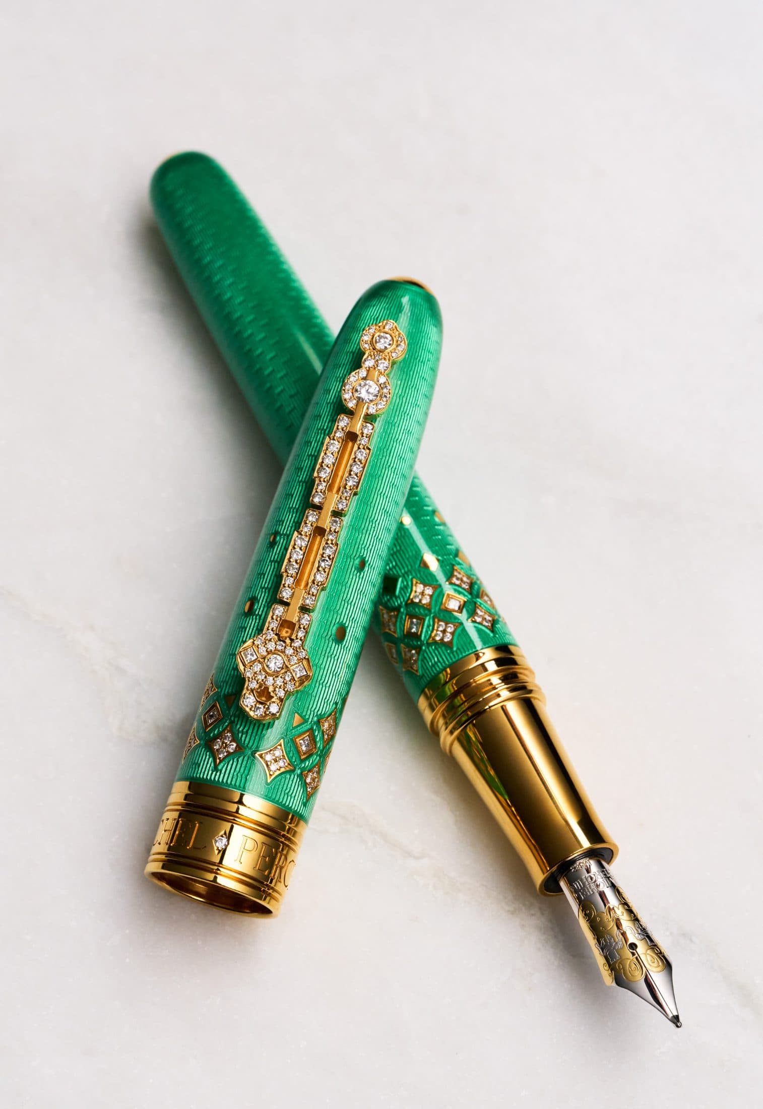 Two Michel Perchin Majesty green guilloche enamel fountain pens crossed, diamond-set clips and lattice collars, on Carrara marble