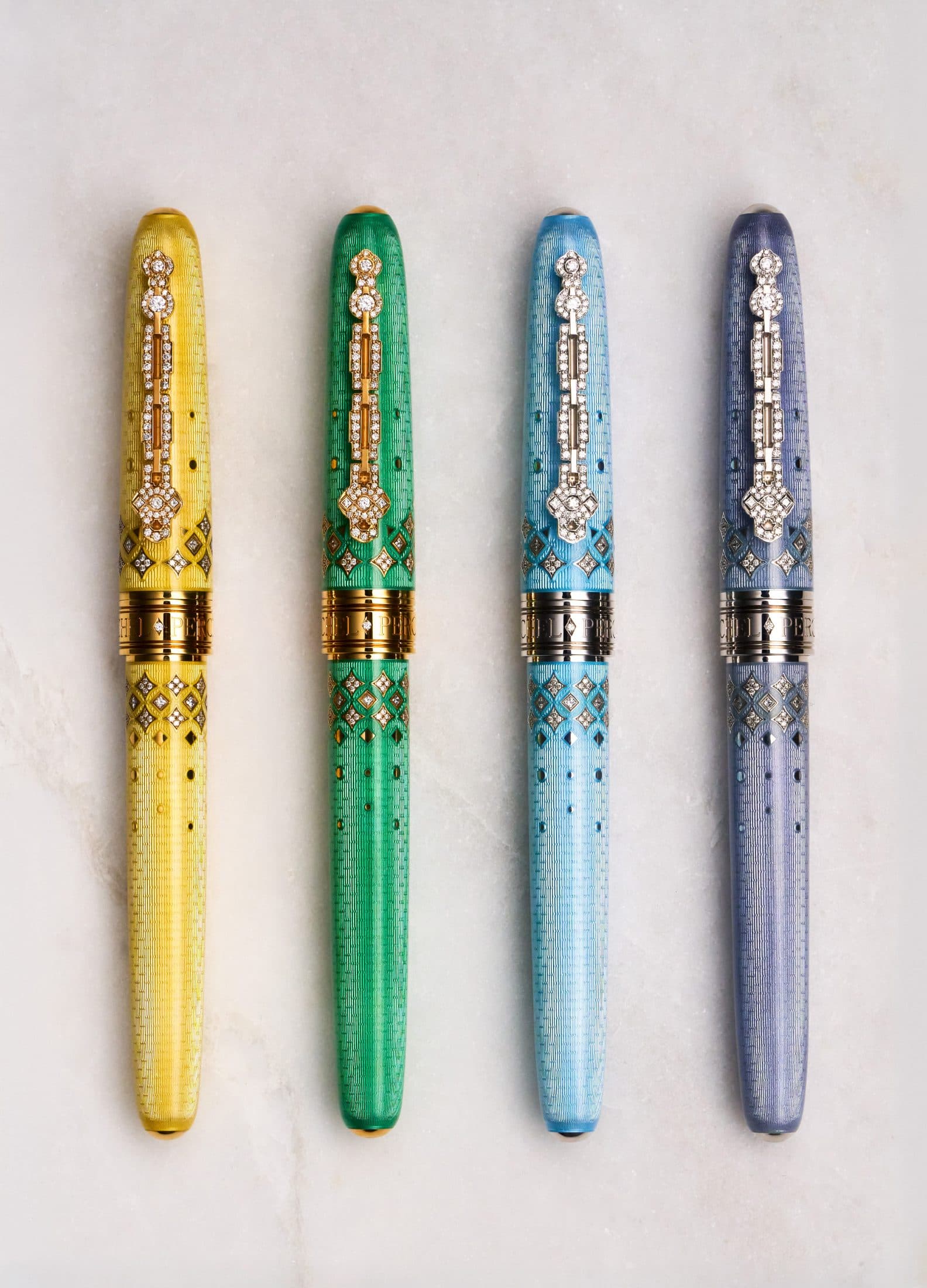 The four Michel Perchin Majesty colourways standing in a row, each with a diamond-set clip, on Carrara marble