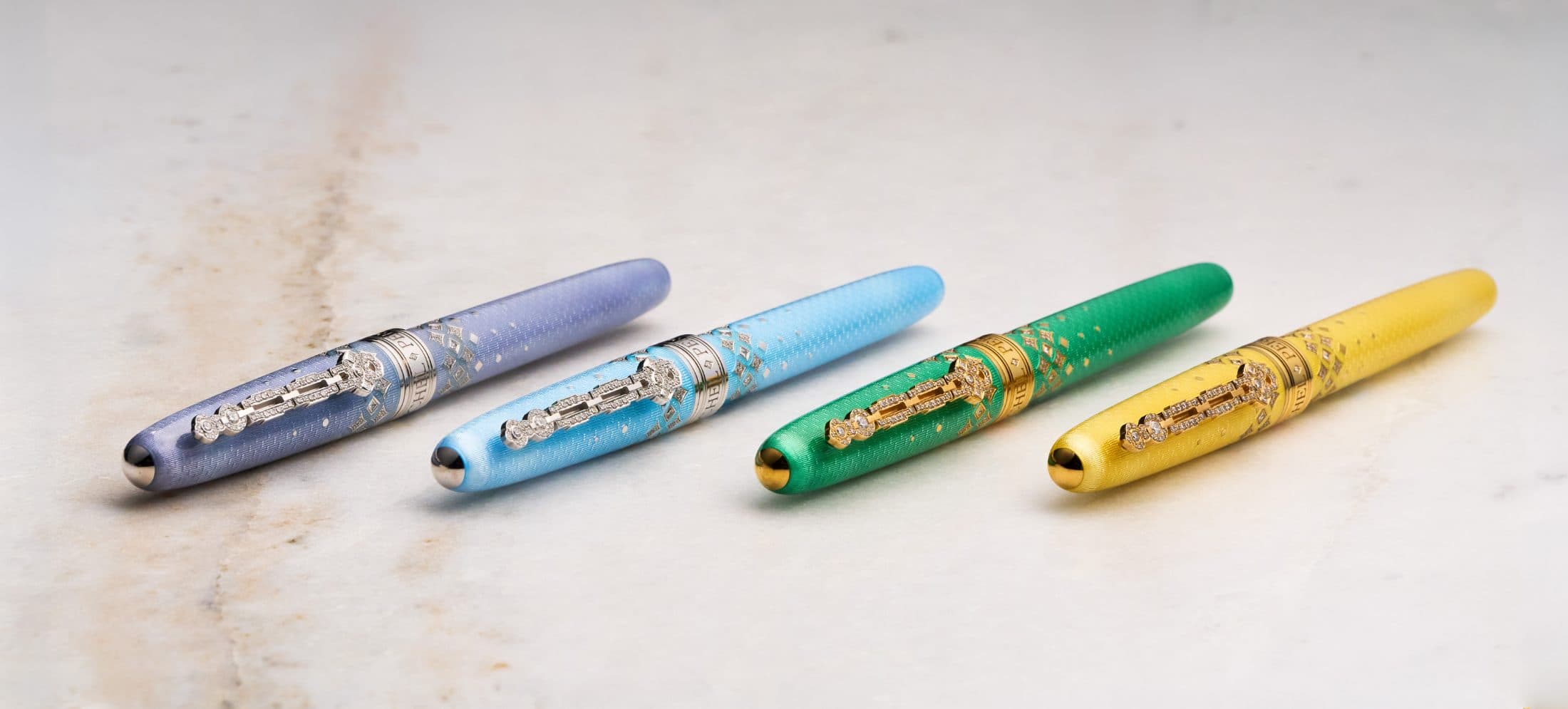 The four Michel Perchin Majesty colourways reclined in a row, diamond-set caps, on Carrara marble