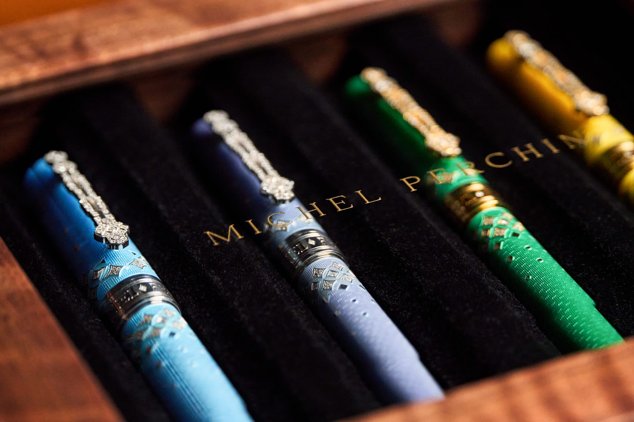 The four Michel Perchin Majesty colourways resting in a burl and velvet presentation case with gold-leaf house name