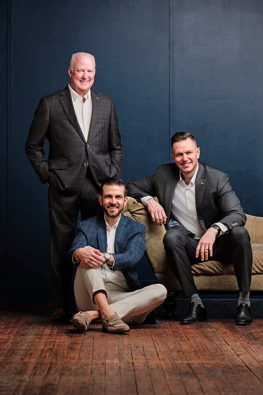 Executive team of three professionals in matching dark suits photographed against neutral backdrop with three-point studio lighting