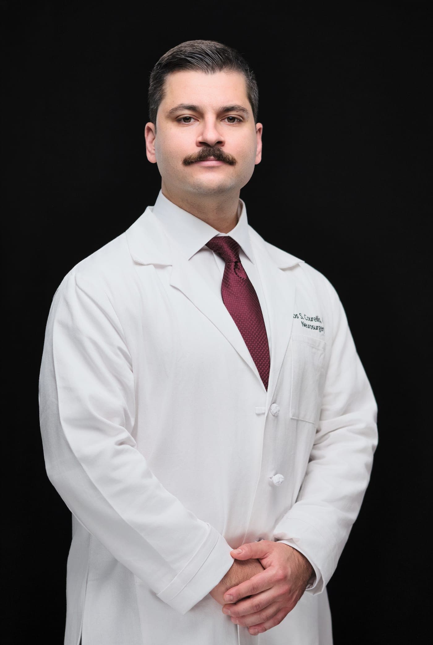 Washington University neurosurgery team member in a WashU Medicine white coat, studio headshot on black in St. Louis by Henry David Photography